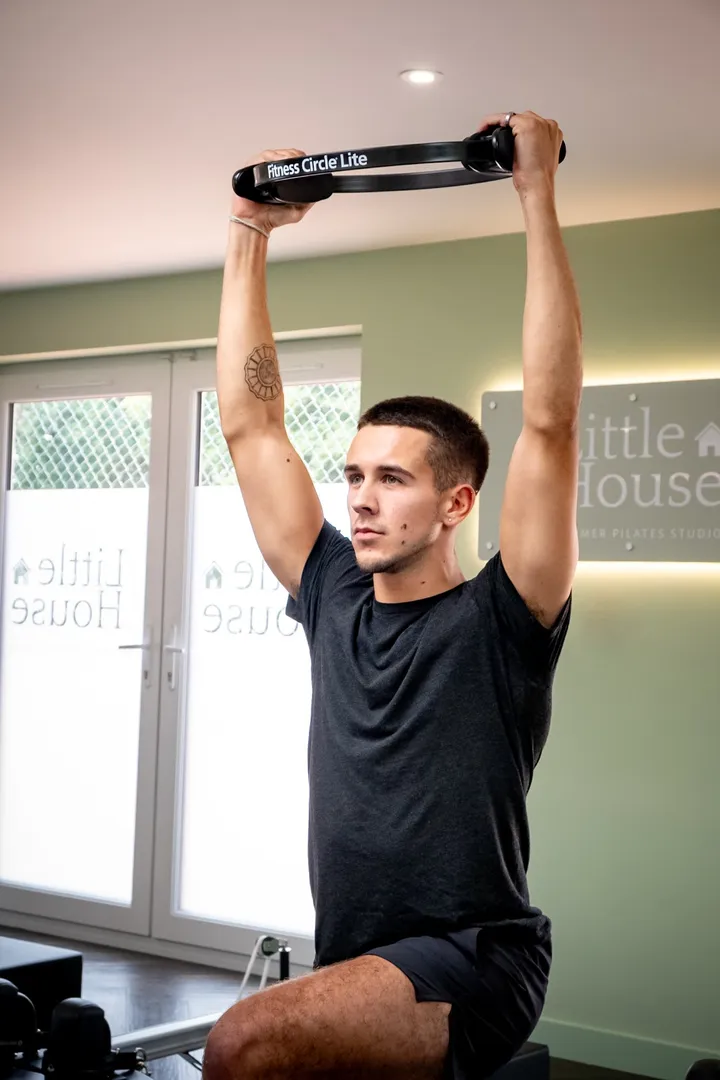 Alex holding a Pilates ring overhead on a reformer