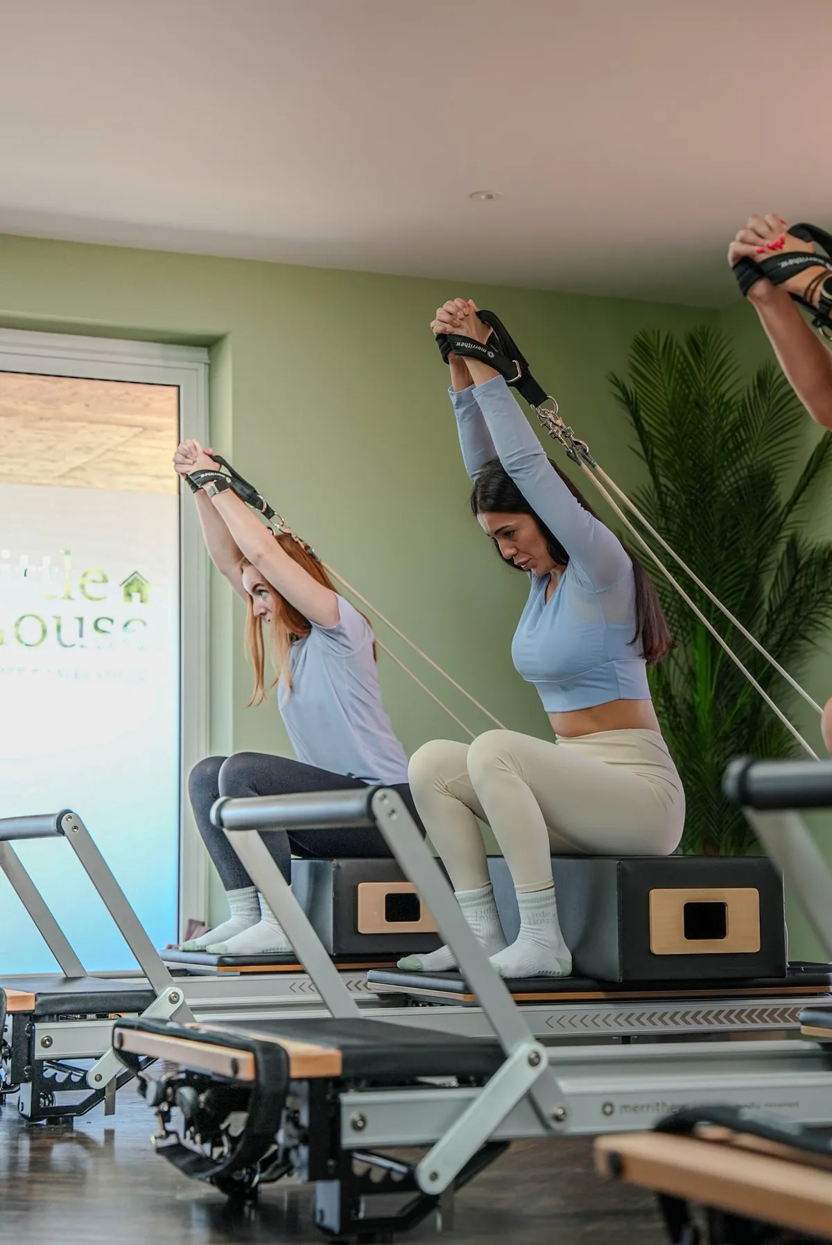 Two people seated on reformers with arms raised during an LH Basic Classical class at Little House Pilates
